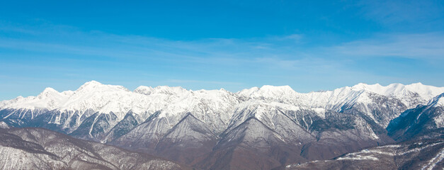 Wide panorama view of mountain peaks in winter season with clear cloudless weather.