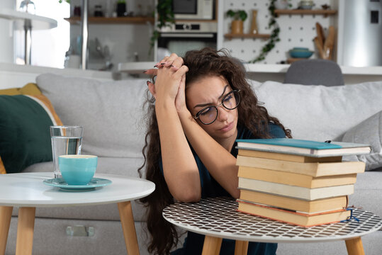 Young schoolgirl or university student has a headache when she sees how much she has to study in order to prepare for the exam and achieve knowledge after illness and absence from classes and lectures