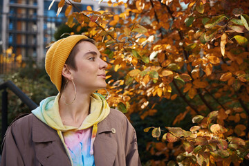 Fototapeta na wymiar Young woman stands against backdrop of autumn tree and skyscrapers