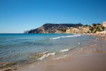 Fototapeta na wymiar Panorámica de la playa del pueblo de Calpe con el cristalino mar Mediterráneo finalizando en la arena con la zona montañosa al fondo.