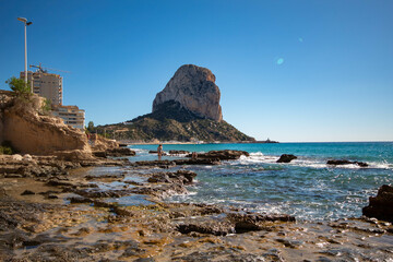 Panorámica del peñón del pueblo de Calpe en Alicante en una zona rocosa de la playa con el mar Mediterráneo bajo un cielo soleado azul.