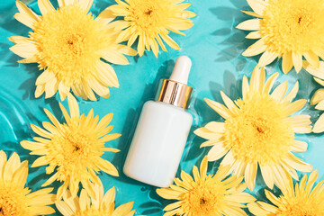 White cosmetic serum dropper bottle with yellow chrysanthemum flowers on blue water background with...