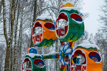 Attraction for children in the park in winter. Mini ferris wheel. Snow on the attraction. Against the background of trees. Close-up