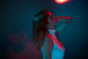 Portrait of young beautiful woman posing, dancing isolated over blue studio background in red neon light. Lifestyle