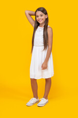 positive teen girl in white dress standing on yellow background