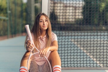 Attractive young fit caucasian female in pink athleisure posing with a tennis racket on a court
