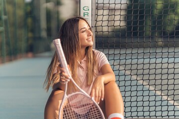 Attractive young caucasian female in pink athleisure posing with a pink racket on a tennis court