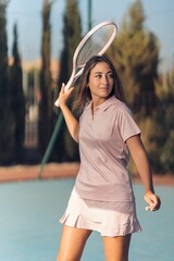 Vertical shot of a young female in pink athleisure playing tennis with a pink racket on a court