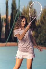 Vertical shot of a young female in pink athleisure playing tennis with a pink racket on a court