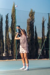 Vertical shot of young female in pink athleisure serving a ball with a pink racket on a tennis court