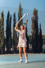 Vertical shot of young female in pink athleisure serving a ball with a pink racket on a tennis court