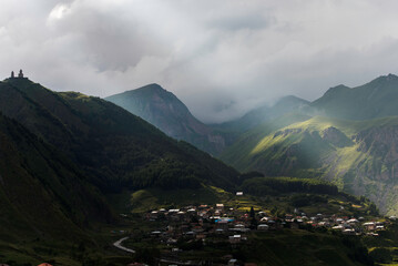 Gruzja widok latem w stronę góry Kazbek przy częściowym zachmurzeniu. , a poniżej wioska Stepancminda - obrazy, fototapety, plakaty