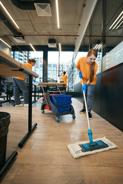 Team cleaning ladies works in coworking area, women use mop, buckets, rags