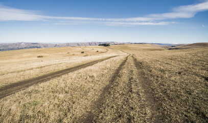 Earthen road on mountain hills among the grass in sunny weather in autumn, rural road in autumn in October