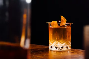 Foto op Plexiglas old fashioned cocktail glass between bottles in a bar © Heleno