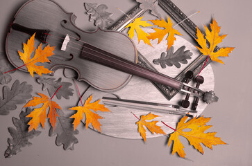 Violin with a bow, art palette and brushes on a wooden background with autumn maple leaves.