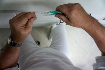 Hände von Arzt beim Aufziehen von medizinischer Spritze in Arztpraxis 