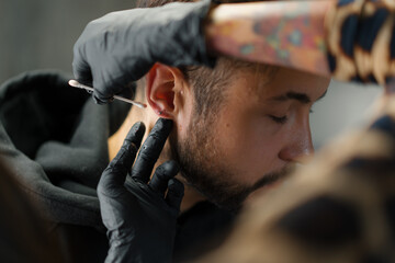 Tattoo piercing studio - a woman makes an ear piercing to a man to a guy