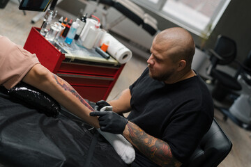Fototapeta na wymiar Close-up - the process of tattooing a woman on her leg. Male tattoo artist making a tattoo