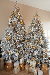 Vertical photo of two huge rich christmas tree with many presents in white, gold and silver color at cozy home. Luxury interior decorated for winter holidays.