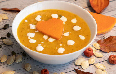 pumpkin cream soup in white bowl and seeds on a table, selective focus 