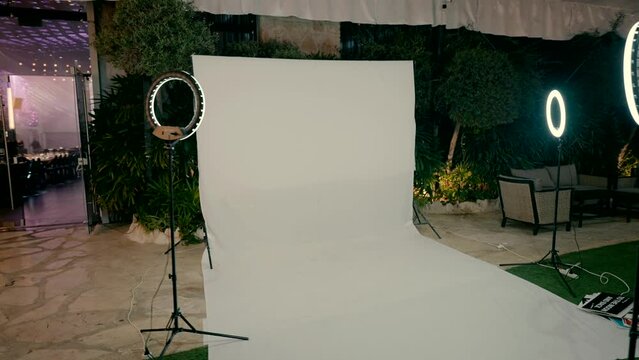 A white background made of white paper stands at the entrance to the event hall for taking photos of guests. White background for wedding photos. LED lamps for photography. Studio.