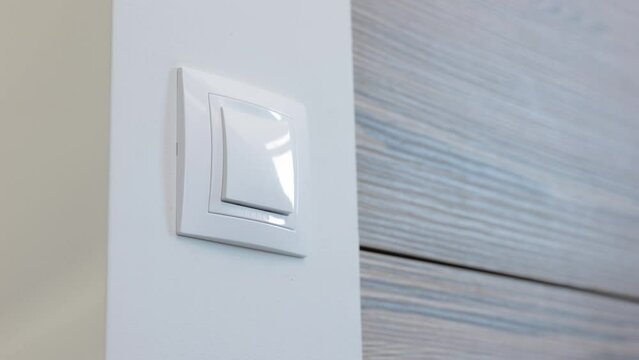 Hand of woman presses buttons of white switch on wall to turn off light. Female guest switches off illumination before leaving hotel room close view