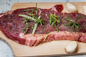 Seasoned raw sirloin beef steak on cutting board with thyme rosemary and garlic