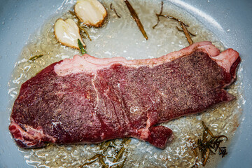 Seasoned sirloin steak grilled on pan with butter, thyme, rosemary and garlic