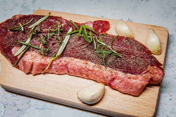 Seasoned raw sirloin beef steak on cutting board with thyme rosemary and garlic