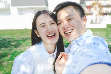 Young smiling couple taking selfie with smartphone outdoors-Happy Asian teenagers looking at camera and having fun at park- Portrait of japanese people-Youth culture - Friendship concept