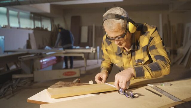 An adult carpenter works in a carpentry shop.
Male carpenter measuring wood board in a carpentry shop.
