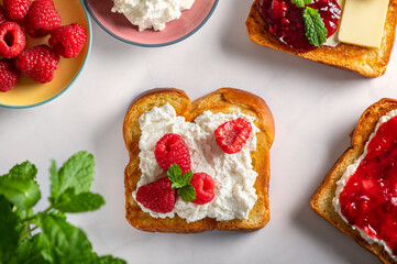 Open Sandwiches fro tasty breakfast with Brioche bread slices, ricotta cheese, butter, fresh raspberries and raspberry jam and mint leaves