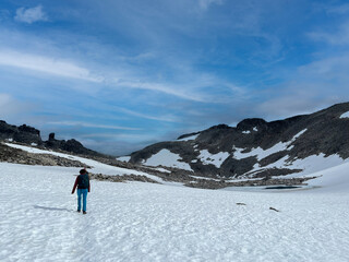 Fototapeta na wymiar woman trekking through the norwegian and snowy nordic mountains with blue sky