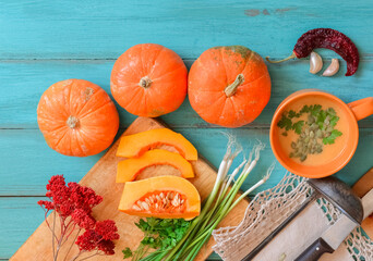 Pumpkin soup on blue wooden table, linen cloth, vintage cutlery. Autumn cream soup, seeds and parsley. Sliced herbs, pumpkin on cutting board, cooking process. Thanksgiving dinner, flat lay, top view.