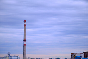 Factory pipe on the background of a beautiful blue sky, with fog or smoke. Evening time