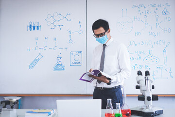 Science teacher wearing mask stands teach science class in the classroom with a microscope chemistry test tube placed in the classroom. The concept of teaching during the Covid-19 situation