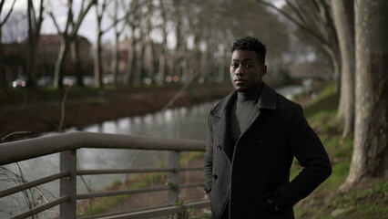 Elegant young black man standing outside at park wearing winter clothing coat