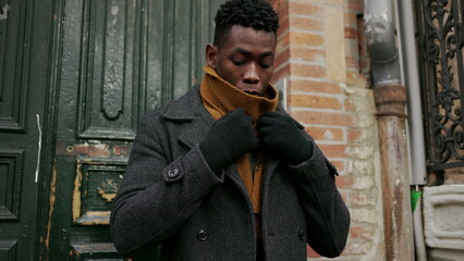 Elegant black man opening home door steps outside in the cold adjusting clothes