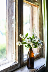 A bottle with blooming jasmine branches by the window in a rustic house