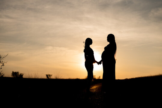 Silhouette of a pregnant lady standing with her partner in a field of long grass