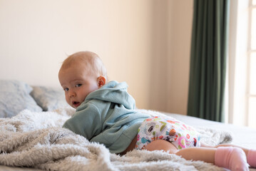A happy, content baby lying on her stomach doing tummy time to strengthen her back. She is wearing a modern, reusable cloth diaper