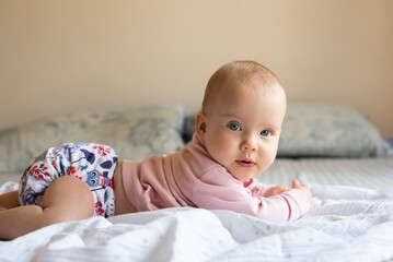 A happy, content baby lying on her stomach doing tummy time to strengthen her back. She is wearing a modern, reusable cloth diaper - obrazy, fototapety, plakaty