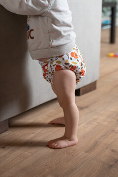 A baby girl learning how to stand up. She is wearing a modern, reusable cloth diaper
