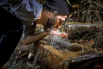 Mann mit Bart trinkt frisches Quellwasser direkt aus dem Brunnen im Wald