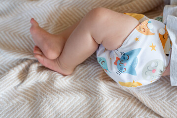 A baby lying on a bed with the focus on the baby's legs. She is wearing a modern, reusable cloth diaper with a pretty print.