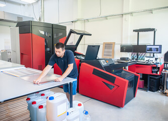 Professional worker with modern big offset printing machine in print house. Printing industry...
