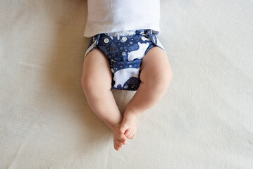 A baby lying on a bed with the focus on the baby's legs. She is wearing a modern, reusable cloth...