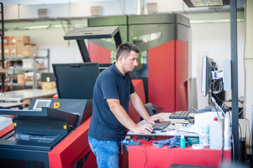 Professional worker with modern big offset printing machine in print house. Printing industry...