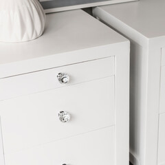 Close-up from a high angle view of a pair of white bed tables next to a white wall in a room under natural lighting.